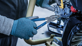 Person wearing safety equipment uses pliers to grip a metal component.