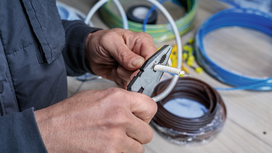 Person strips insulation from electrical wire with pliers on a workbench.