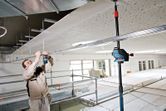 A person wearing safety equipment uses a high-performance receiver to align ceiling structures.