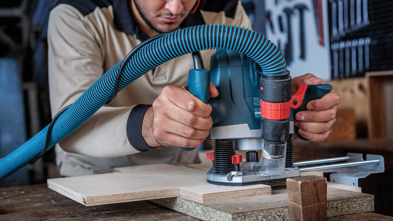 Person wearing safety equipment uses a router to cut a groove in a wood panel.