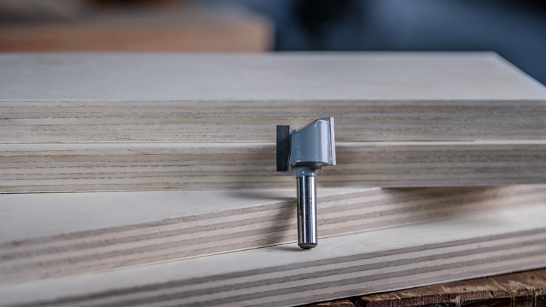Router bit standing upright on stacked plywood boards.