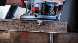 Person using a wood router to shape the edge of a wooden board.