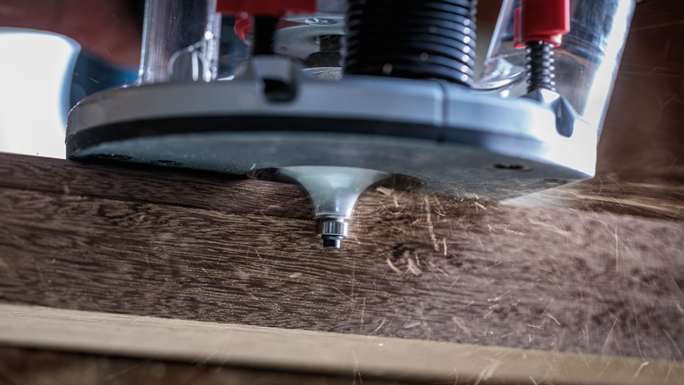 Wood router shaping the edge of a plank, creating wood shavings.