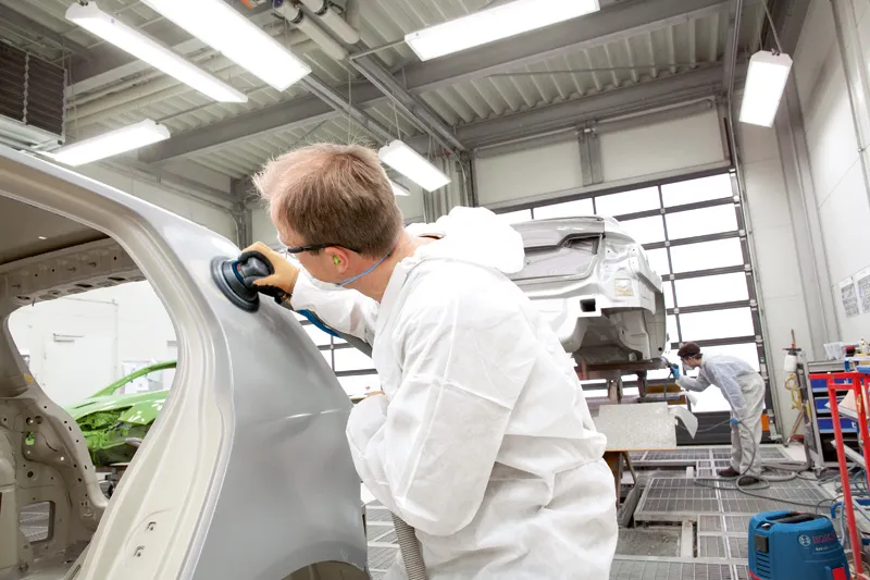 A person wearing safety equipment polishes a car body in a workshop.