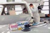 A person wearing safety equipment works near a pneumatic sander and sanding discs in an auto shop.